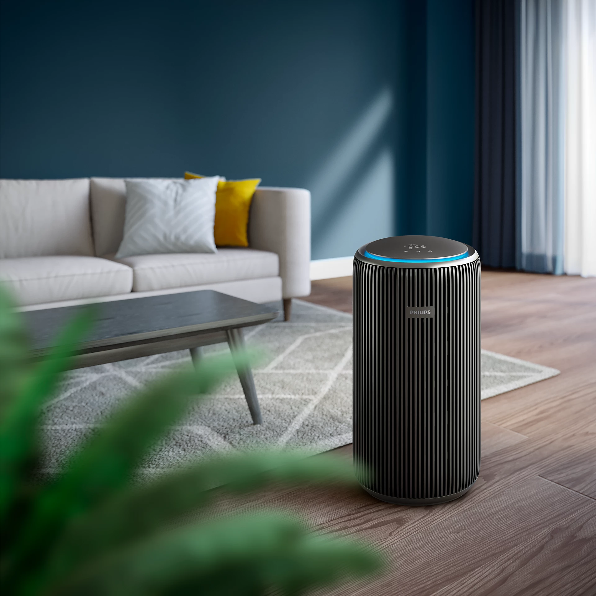 Un purificateur d'air se trouve sur un sol en bois dans un salon. Un canapé avec des oreillers est en arrière-plan.