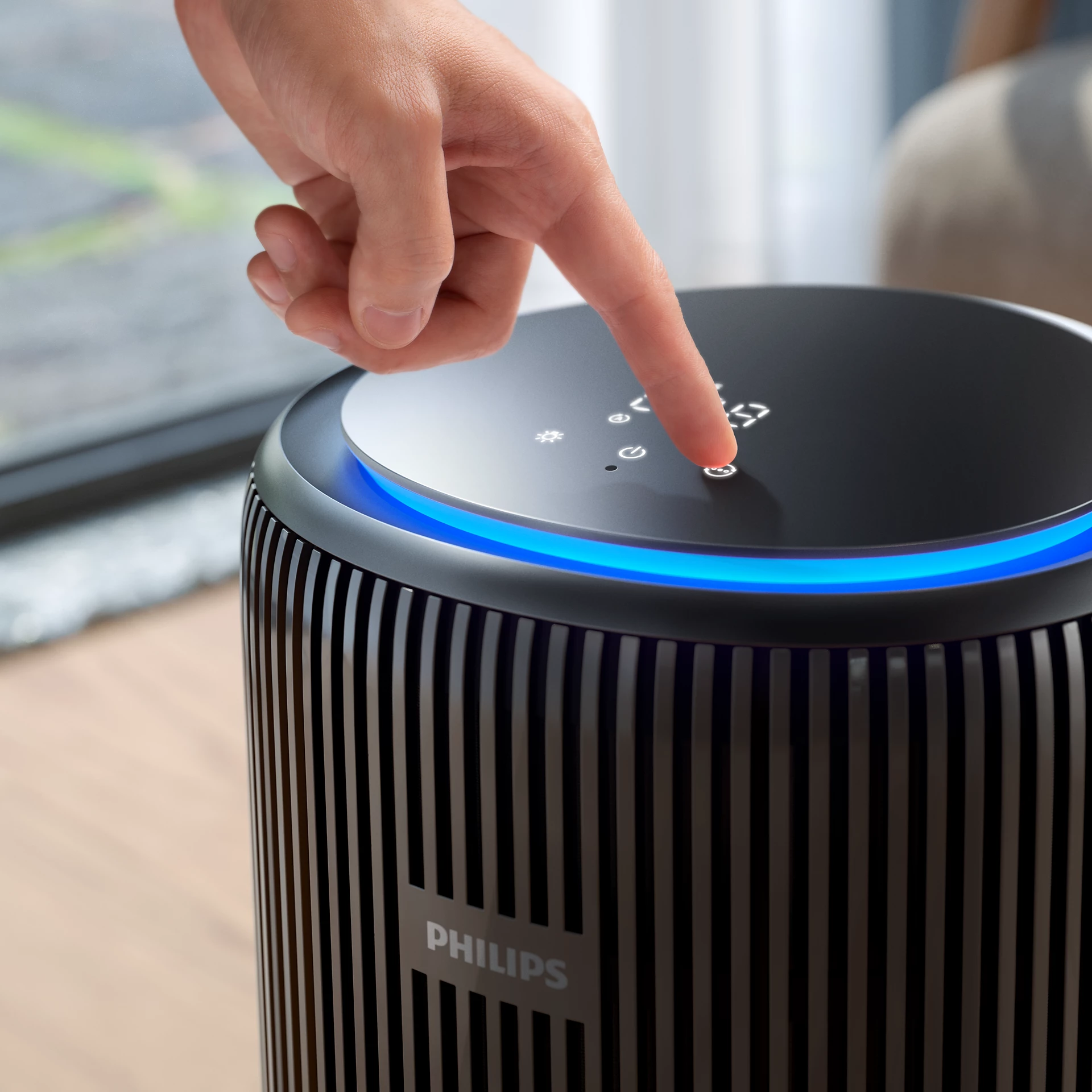 Une main appuie sur un bouton d'un purificateur d'air noir. Le purificateur a une lumière bleue et le logo Philips.