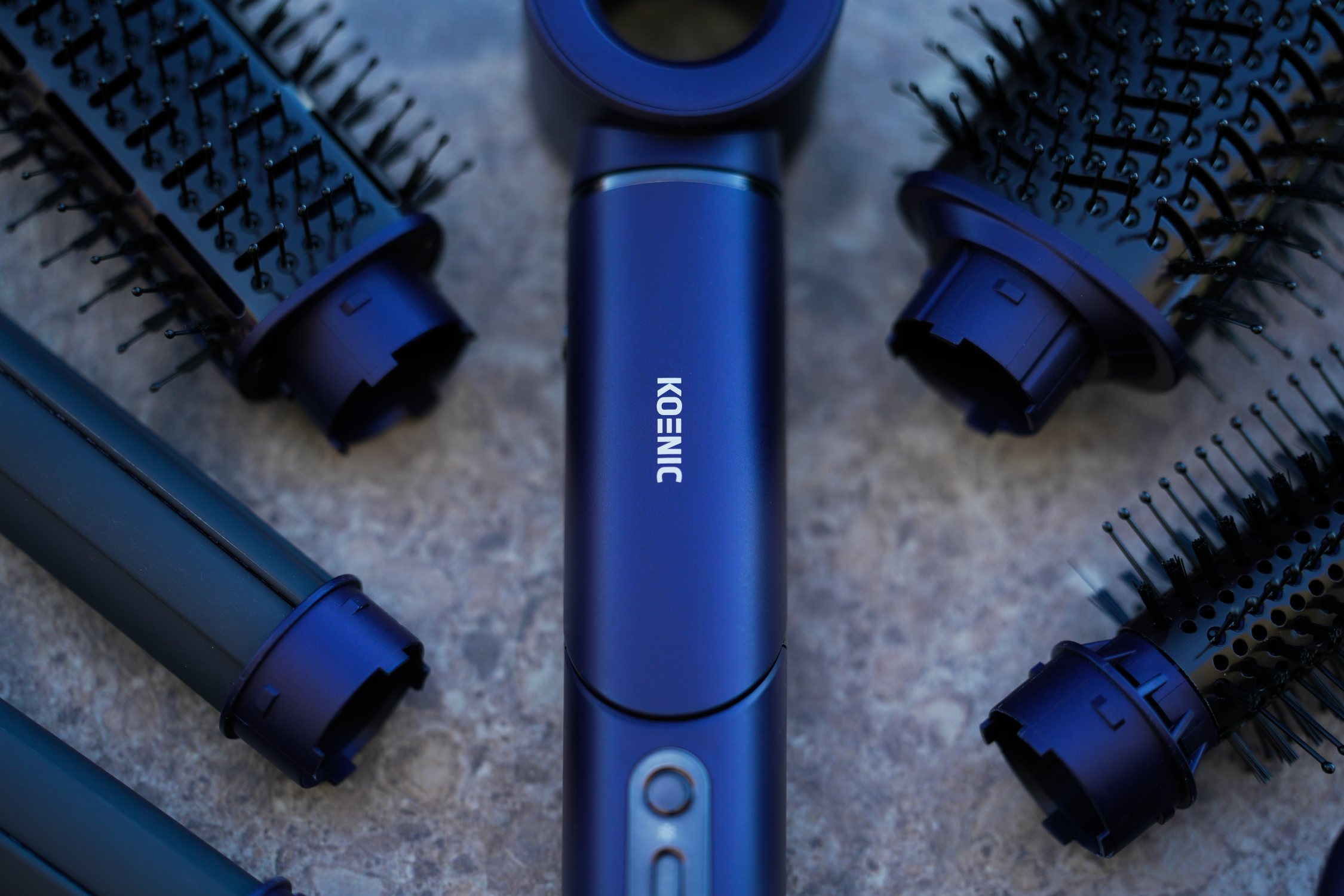Un sèche-cheveux bleu avec accessoires sur une surface en pierre grise. La marque est 'KOENIC'.