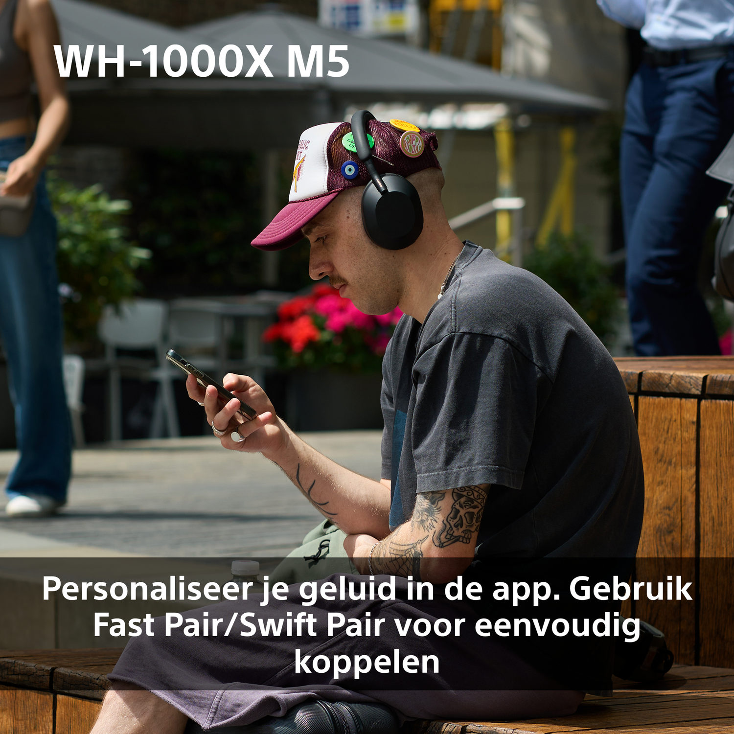 Een man met een koptelefoon en pet kijkt naar zijn telefoon. Hij zit op een houten bank. Tekst: WH-1000XM5 en app-details.