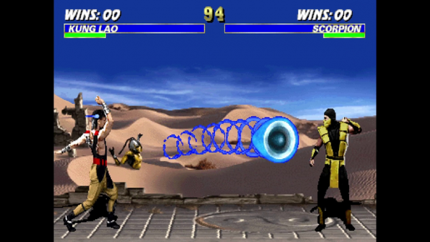 Kung Lao und Scorpion in einem Mortal Kombat-Kampf. Kung Lao wirft ein blaues Energieprojektil. Hintergrund zeigt eine Wüste.