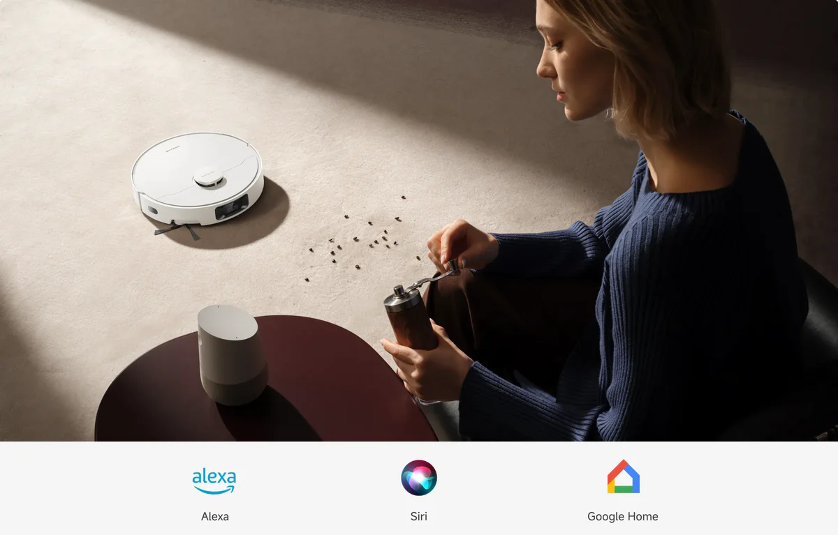 Egy nő kávét őröl, robotporszívó és okoshangszóró van a közelben. Kávébabok szórva. Alexa, Siri és Google Home ikonok.