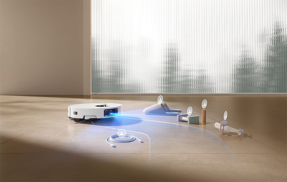 Egy fehér robotporszívó takarít egy szobát. Kék fénye van. Közelben papucsok, egy doboz, egy henger és egy játékrepülőgép látható.