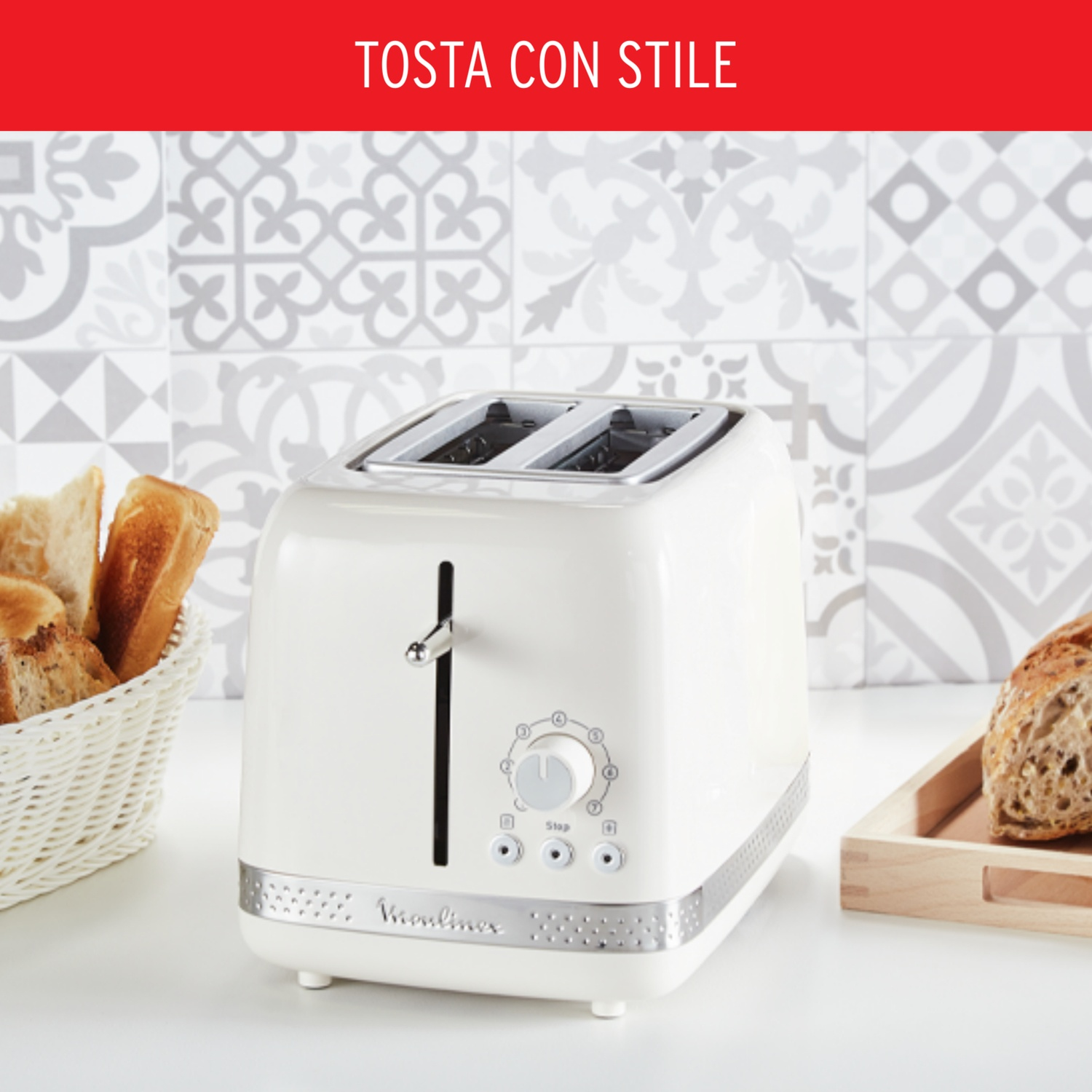 Un tostapane color crema con due fessure è appoggiato su una superficie bianca, con pane in un cestino e su un vassoio. Lo sfondo mostra piastrelle decorate.