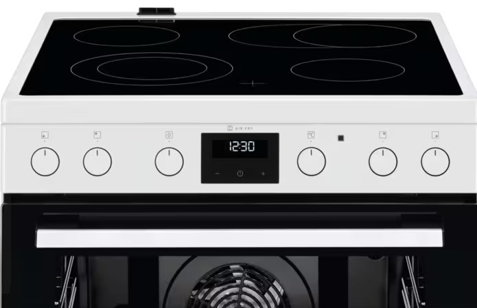Biała i czarna kuchenka elektryczna. Ma czarną płytę grzejną z czterema palnikami, cyfrowy zegar i otwarty piekarnik.