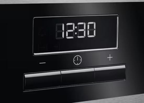 Czarny panel sterowania piekarnika wyświetla godzinę 12:30 na cyfrowym zegarze. Przyciski poniżej obejmują ikonę timera oraz znaki plus i minus.