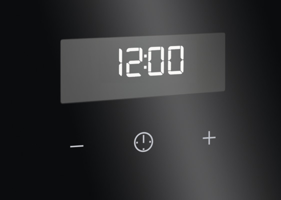 Cyfrowy wyświetlacz pokazuje 12:00. Poniżej symbole minus, zegar i plus na czarnej powierzchni, prawdopodobnie panelu piekarnika.