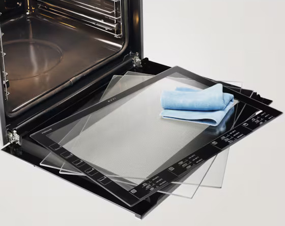 Otwarty piekarnik ze szklanymi panelami i niebieską szmatką. Wnętrze piekarnika jest widoczne. Kilka szklanych płyt z przodu.
