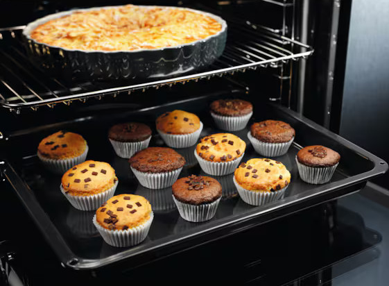Wnętrze piekarnika z wypiekami. Naczynie do zapiekania na górnej półce. Muffiny, niektóre z kawałkami czekolady, na tacy poniżej.
