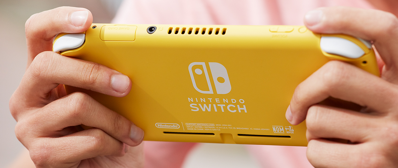 Una persona tiene in mano una Nintendo Switch Lite gialla. Le mani tengono il dispositivo, il logo e la scritta Nintendo Switch sono visibili.