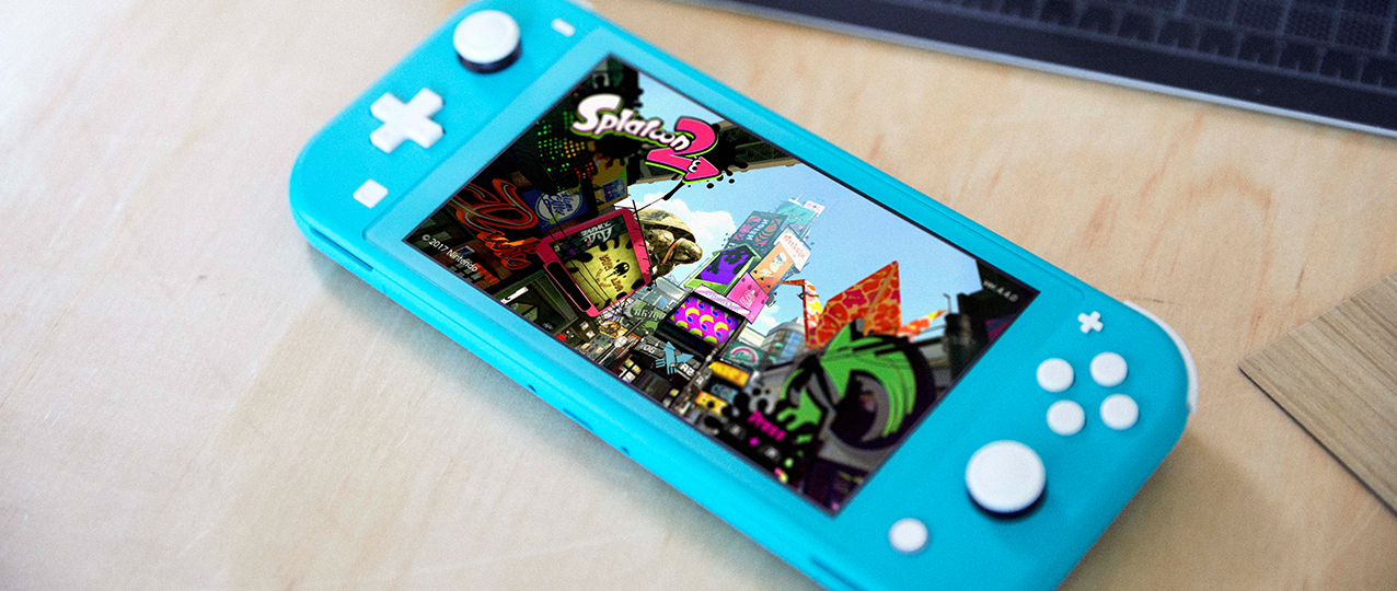 Eine blaue Nintendo Switch Lite mit dem Spiel Splatoon 2. Das Gerät liegt auf einem Holztisch, im Hintergrund eine Tastatur.