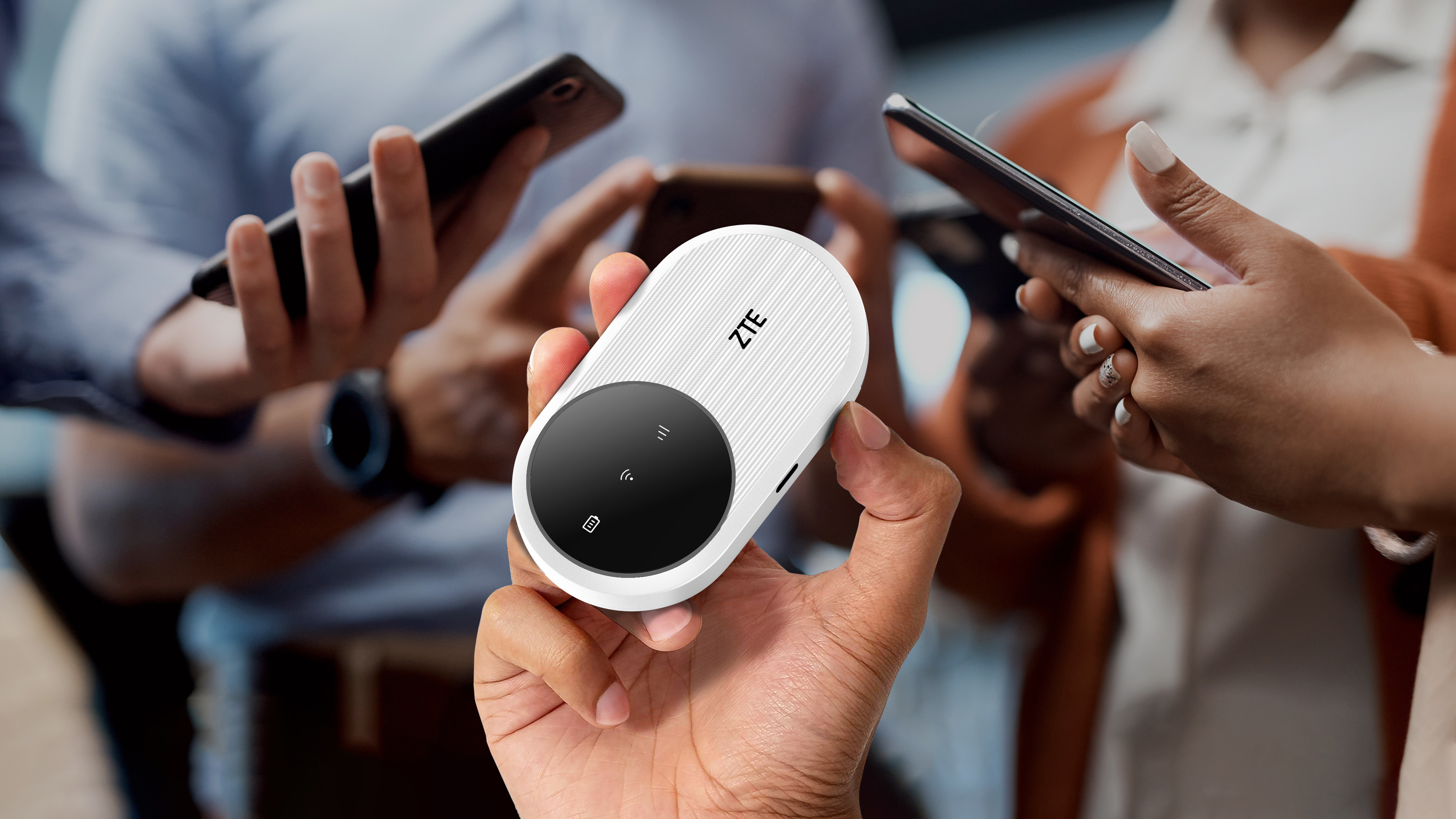 Dłoń trzyma białe urządzenie ZTE z czarnym okręgiem. Inni ludzie używają smartfonów w tle.