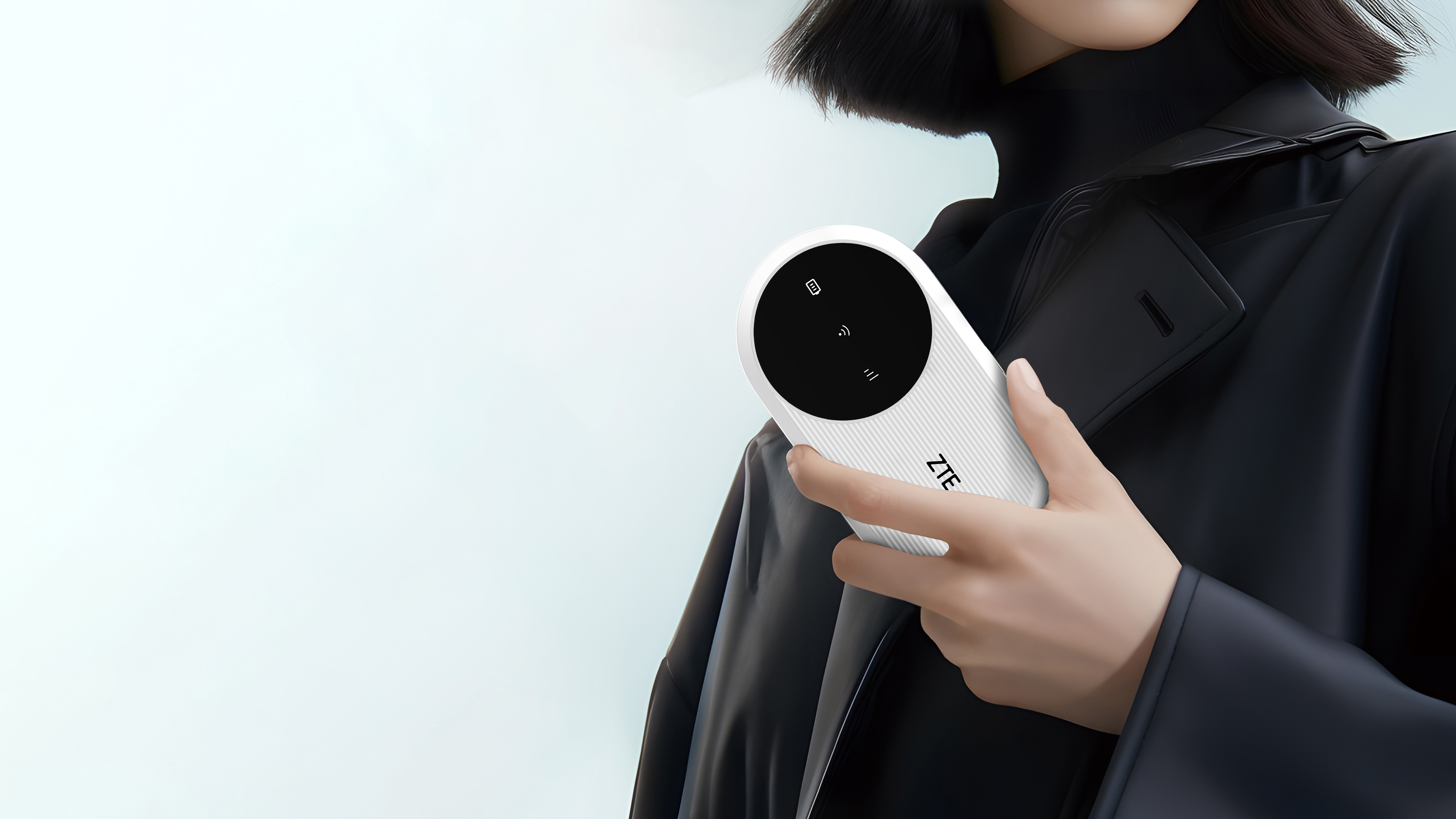 Osoba trzyma białe urządzenie ZTE. Urządzenie ma czarny ekran z ikonami. Osoba ma na sobie czarny płaszcz.