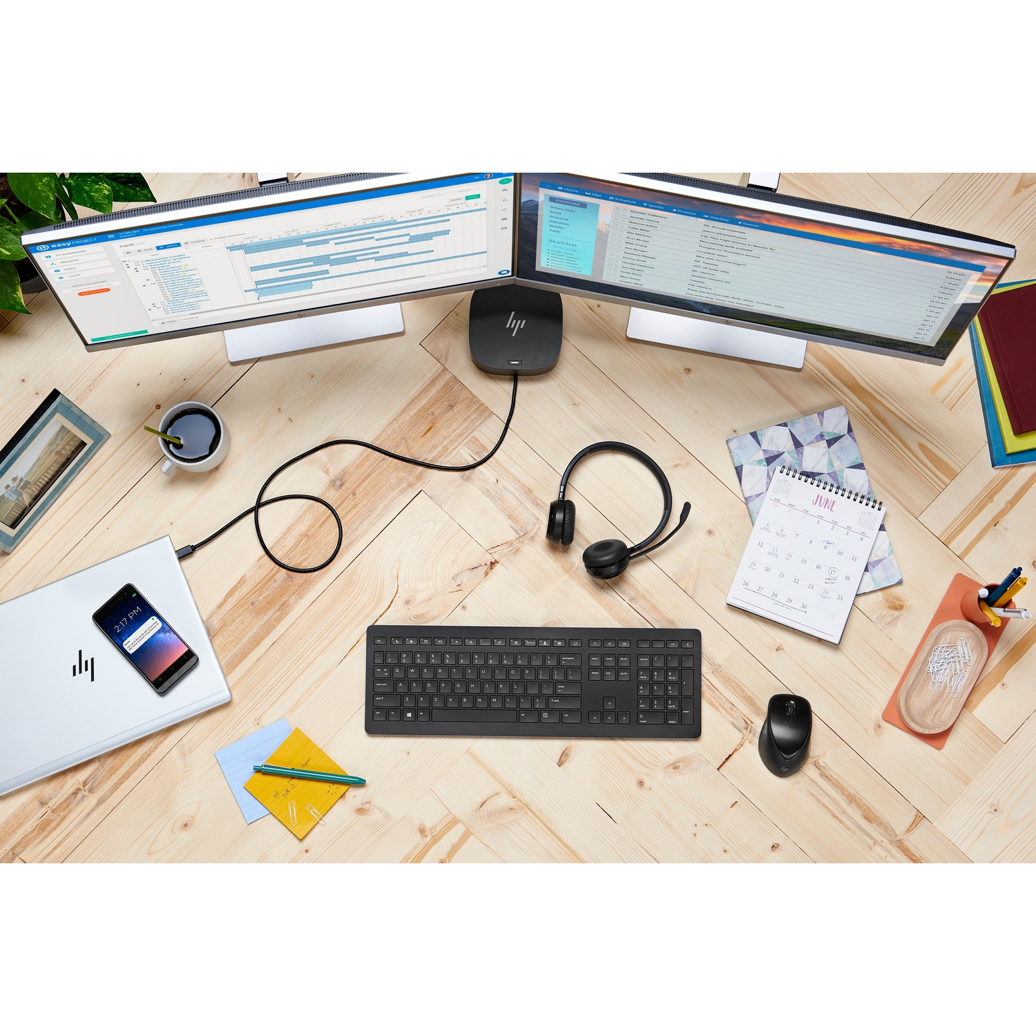 A workspace with two monitors, keyboard, mouse, headset, and a smartphone. A calendar and other office supplies are also present.