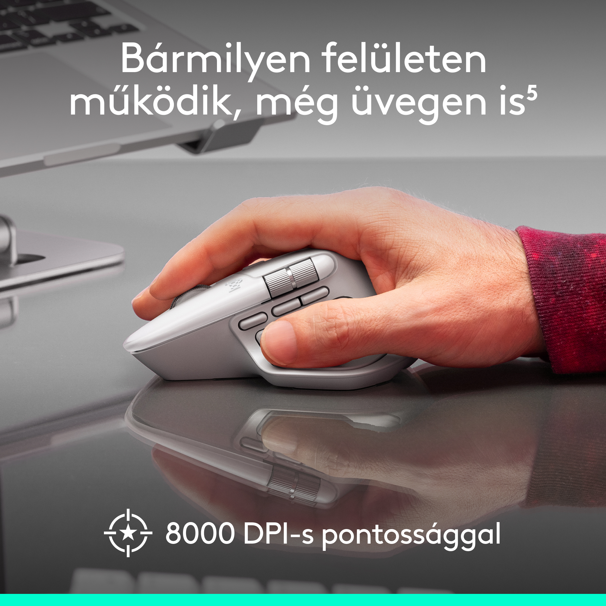 Egy kéz egy szürke számítógépes egeret tart. Az egér egy fényvisszaverő felületen van. A szöveg szerint bármilyen felületen működik, még üvegen is.
