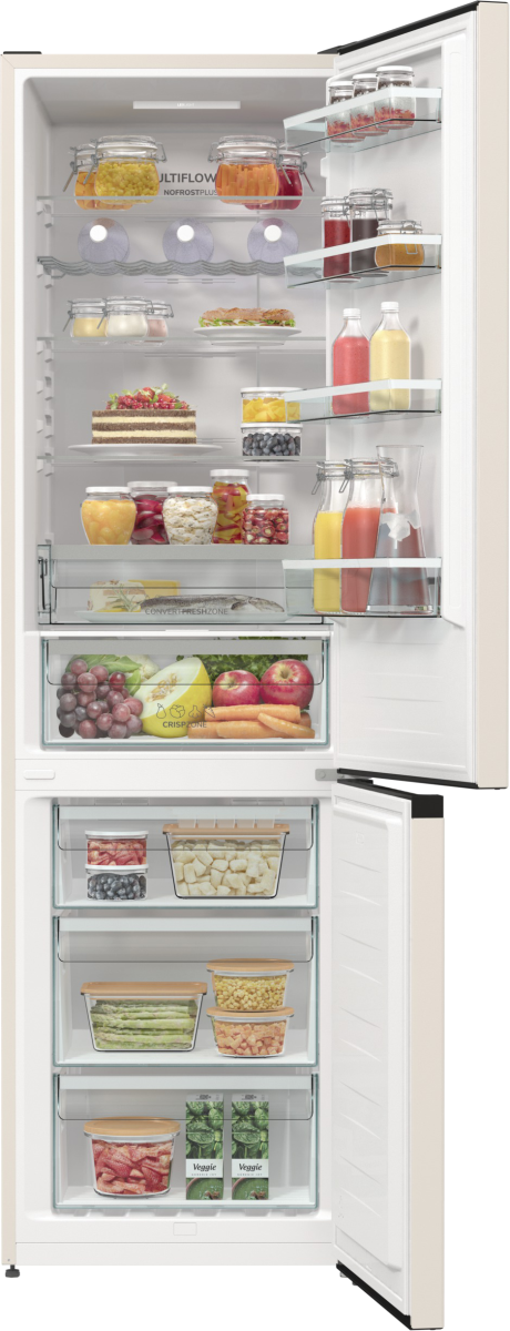 Otwarta lodówka pełna jedzenia. Widoczne słoiki, owoce, warzywa i ciasto. Lodówka jest biała z beżowymi akcentami.