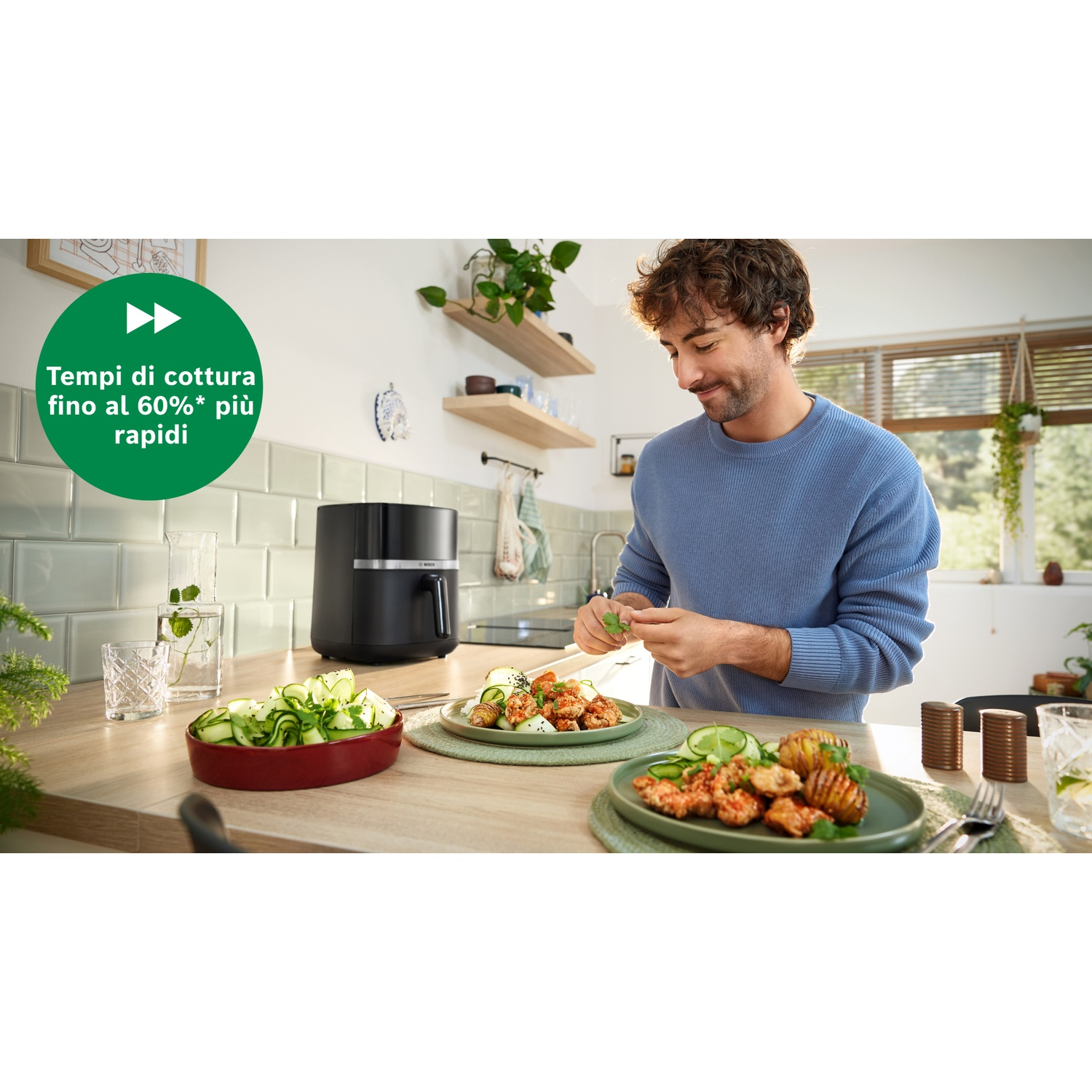 Uomo che prepara il cibo vicino alla friggitrice ad aria. Piatti di cibo e verdure sono sul tavolo. Il testo recita: Tempi di cottura fino al 60% più veloci.