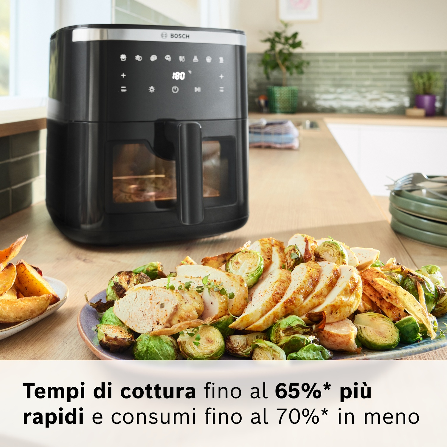 Friggitrice ad aria nera con pollo cotto e cavoletti di Bruxelles su un piatto. Anche patate. Sullo sfondo, cucina.