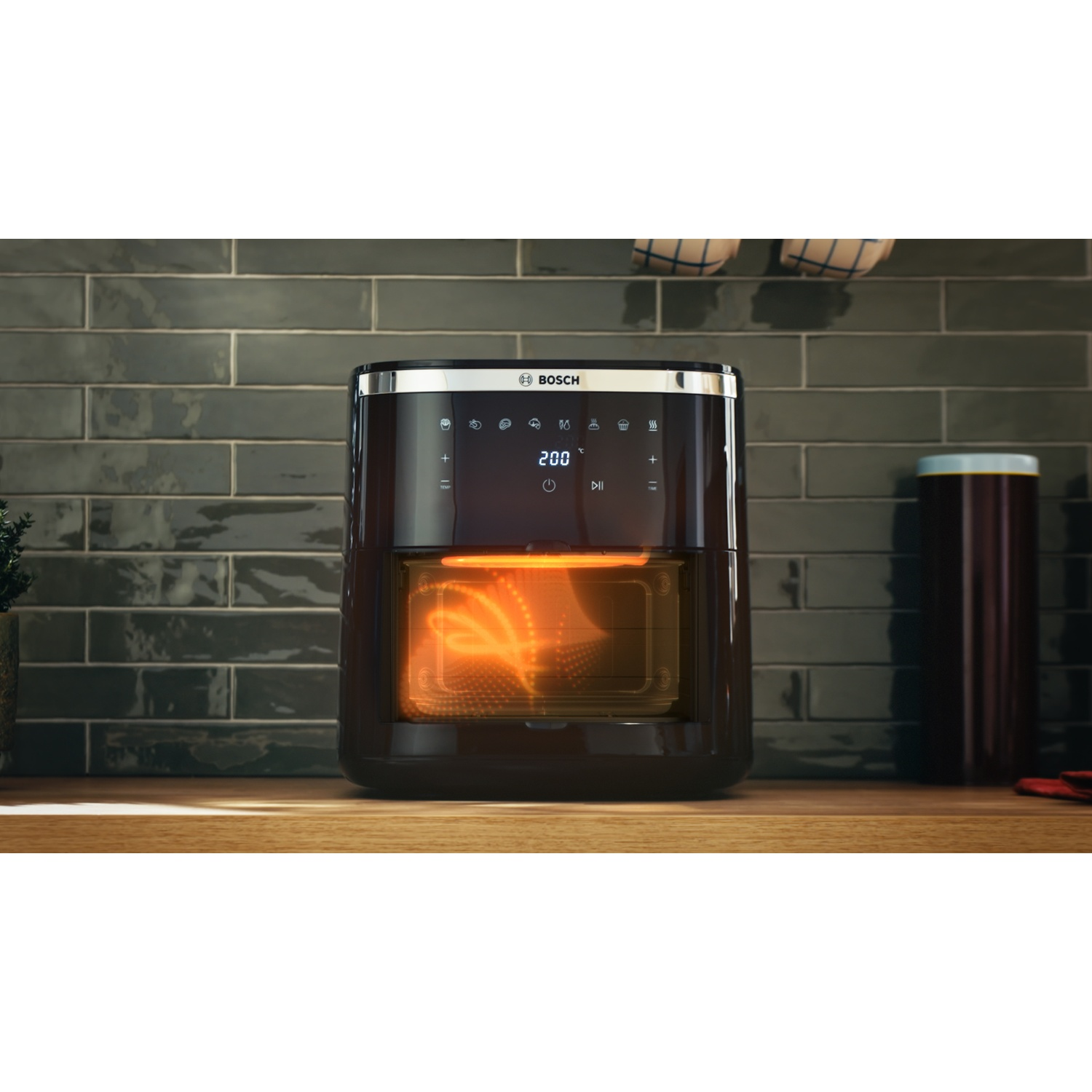 Una friggitrice ad aria nera su un bancone di legno. La friggitrice è accesa, mostrando l'interno luminoso. Sfondo di piastrelle scure con logo Bosch.
