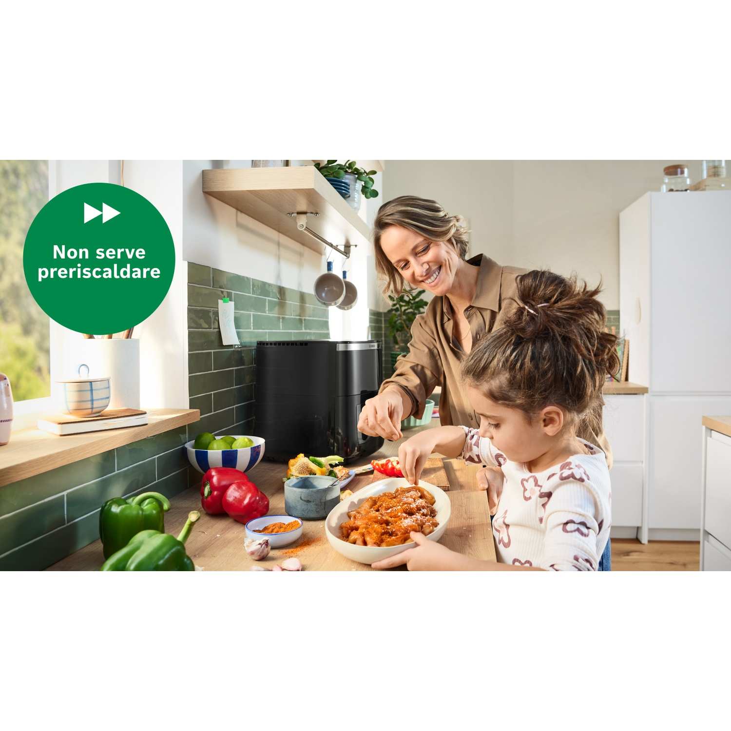 Una donna e una bambina cucinano la pasta. Verdure e una friggitrice ad aria sul bancone. Segno verde dice 'Non serve preriscaldare'.