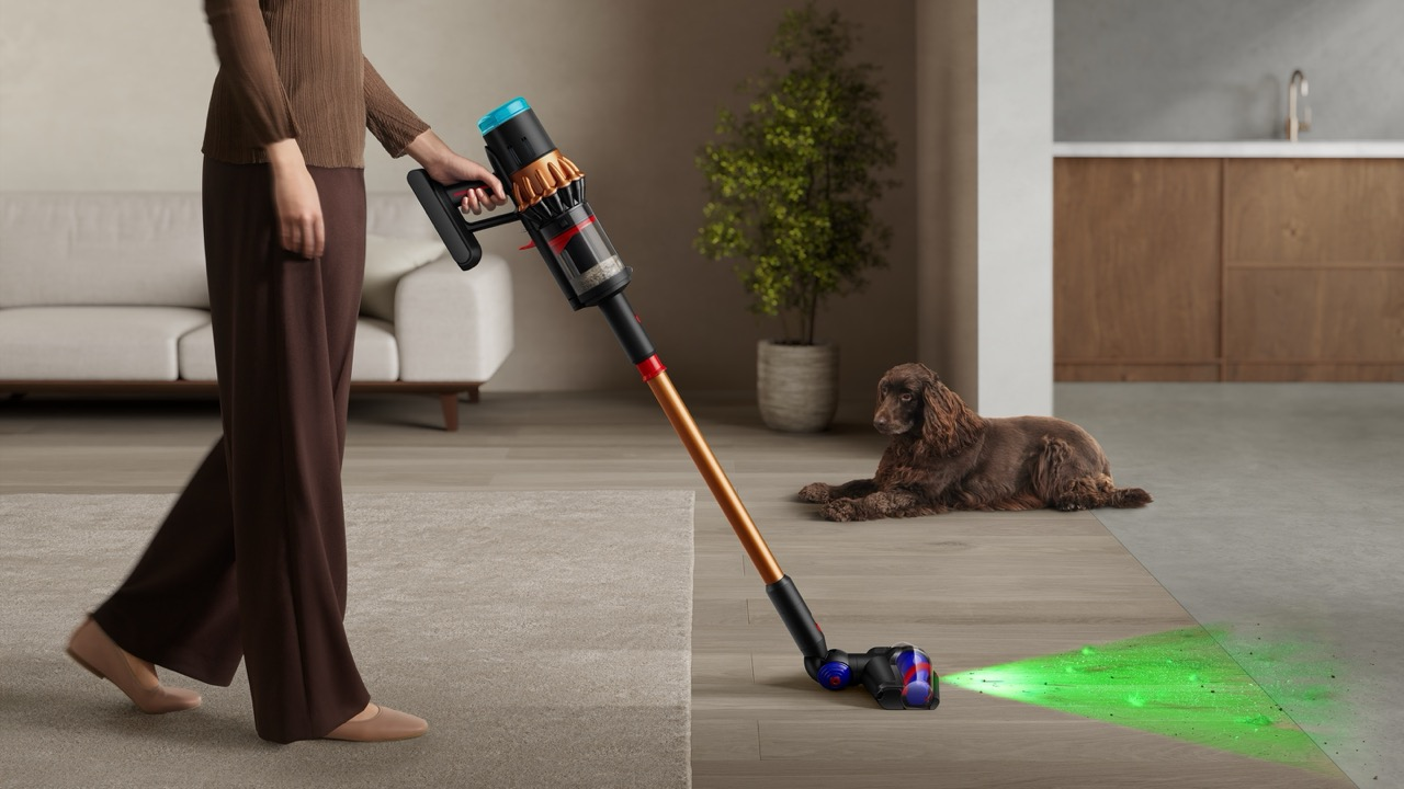 Una persona aspira una habitación. Un perro yace en el suelo. La aspiradora emite una luz verde, resaltando el suelo. Un sofá y una planta están en el fondo.