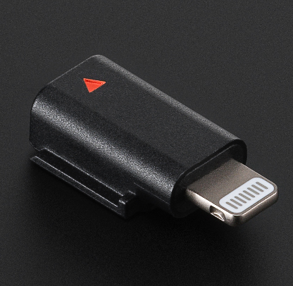 Adaptateur noir avec connecteur argenté. Un triangle rouge sur le dessus. Le fond est sombre.