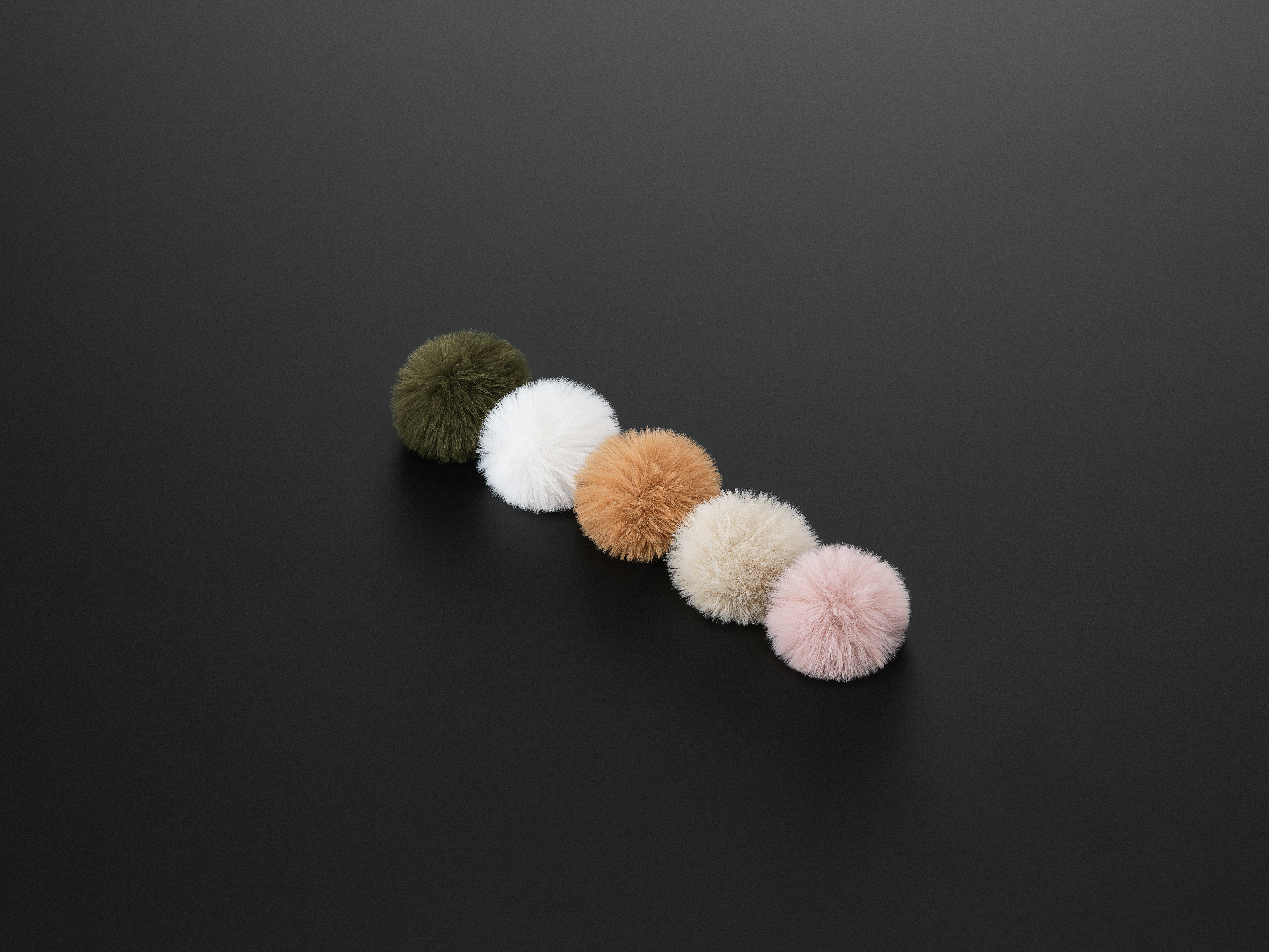 Sei pompon colorati disposti diagonalmente su una superficie nera. I colori includono verde, bianco, beige e rosa.