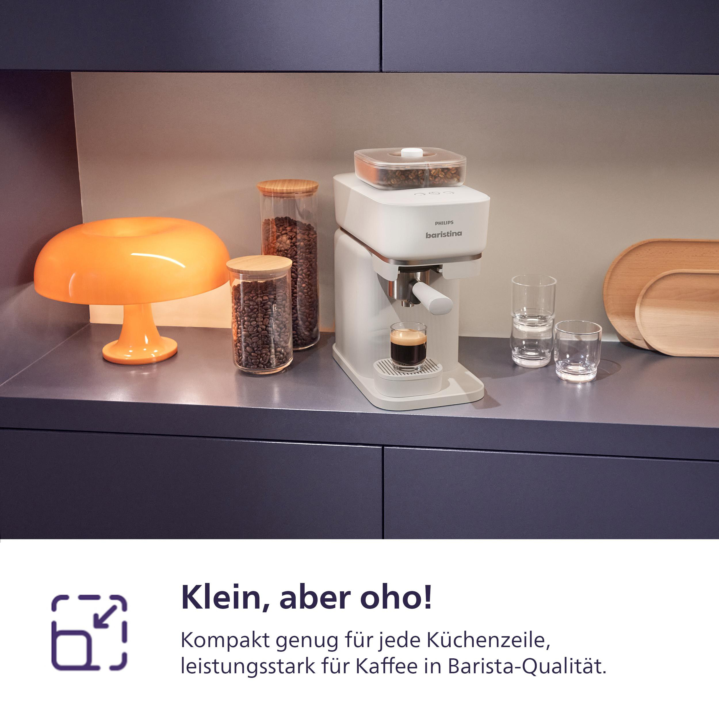 Eine weiße Philips Baristina Kaffeemaschine auf einer Theke. Enthält Kaffeebohnen, eine orangefarbene Lampe, Gläser und Holztabletts.