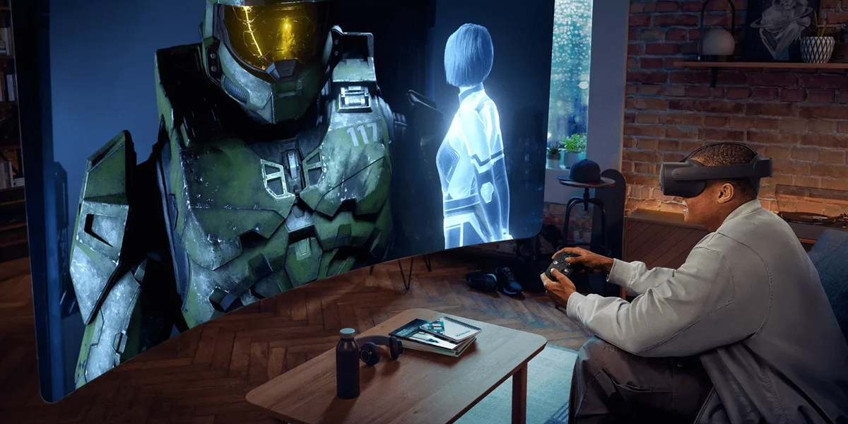 Mężczyzna w zestawie VR gra w grę wideo z postaciami Halo na ekranie. Stół ze słuchawkami i butelką na pierwszym planie.
