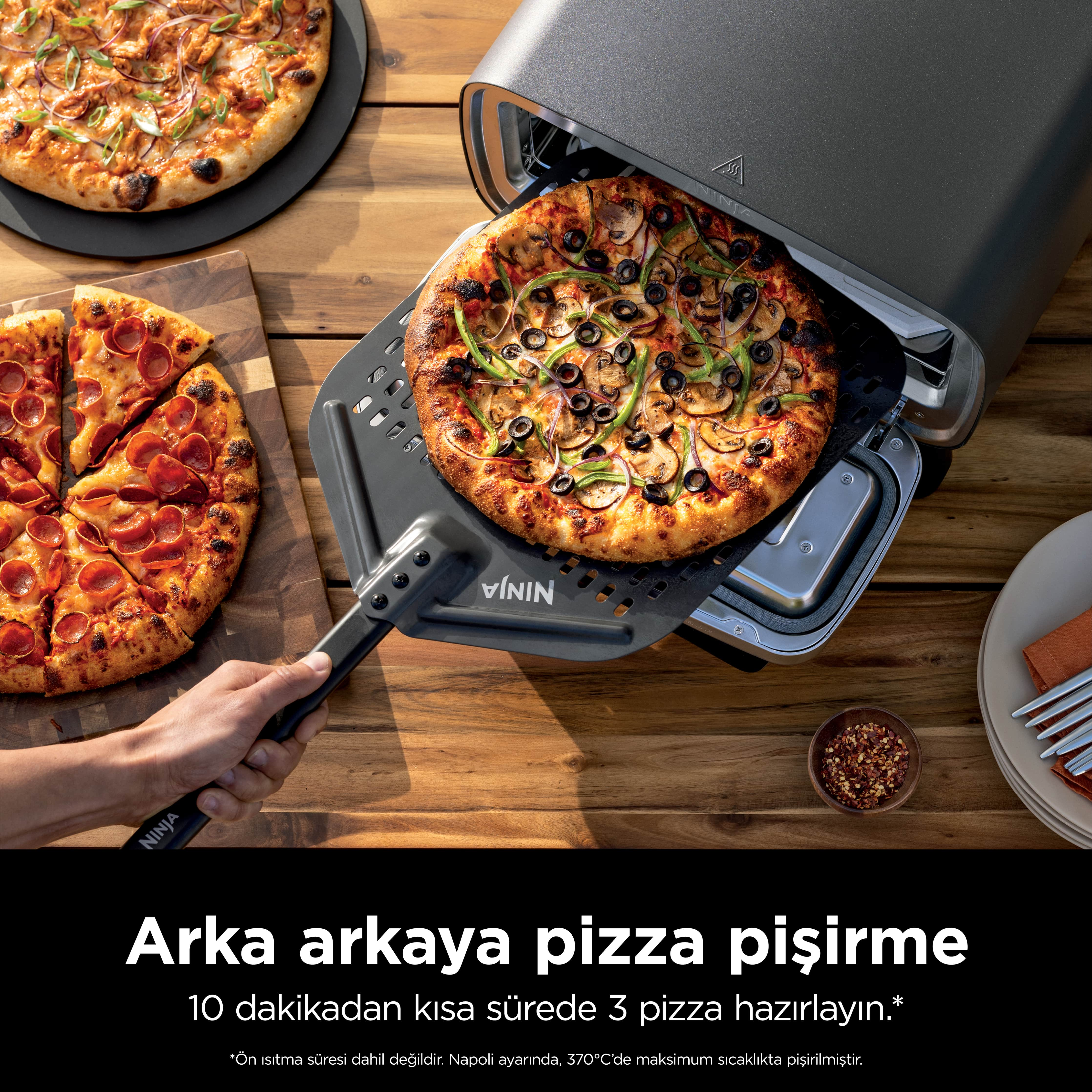 Çıkarılan bir pizzalı pizza fırını. İki pizza kesilmiş ve bir masada. Malzemeler ve tabaklar görülebilir.