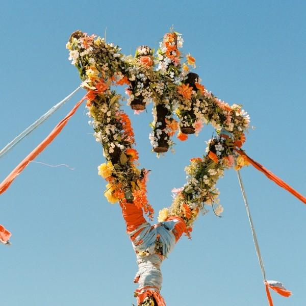 Ein floraler Bogen, verziert mit Blumen und Bändern, steht vor einem klaren blauen Himmel. Der Bogen hat ein einzigartiges, künstlerisches Design.