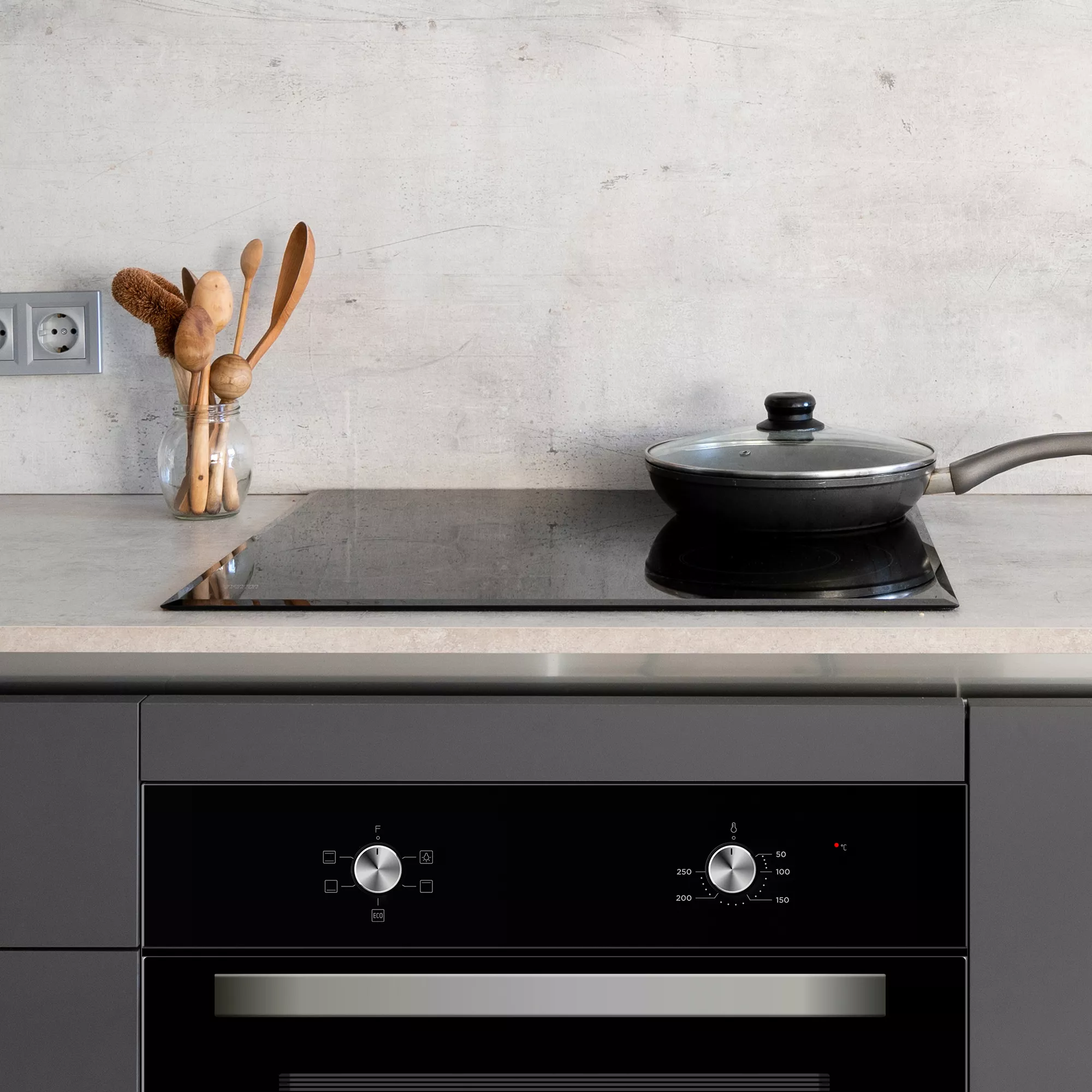 Escena de cocina con cocina negra, sartén, utensilios de madera y horno negro.