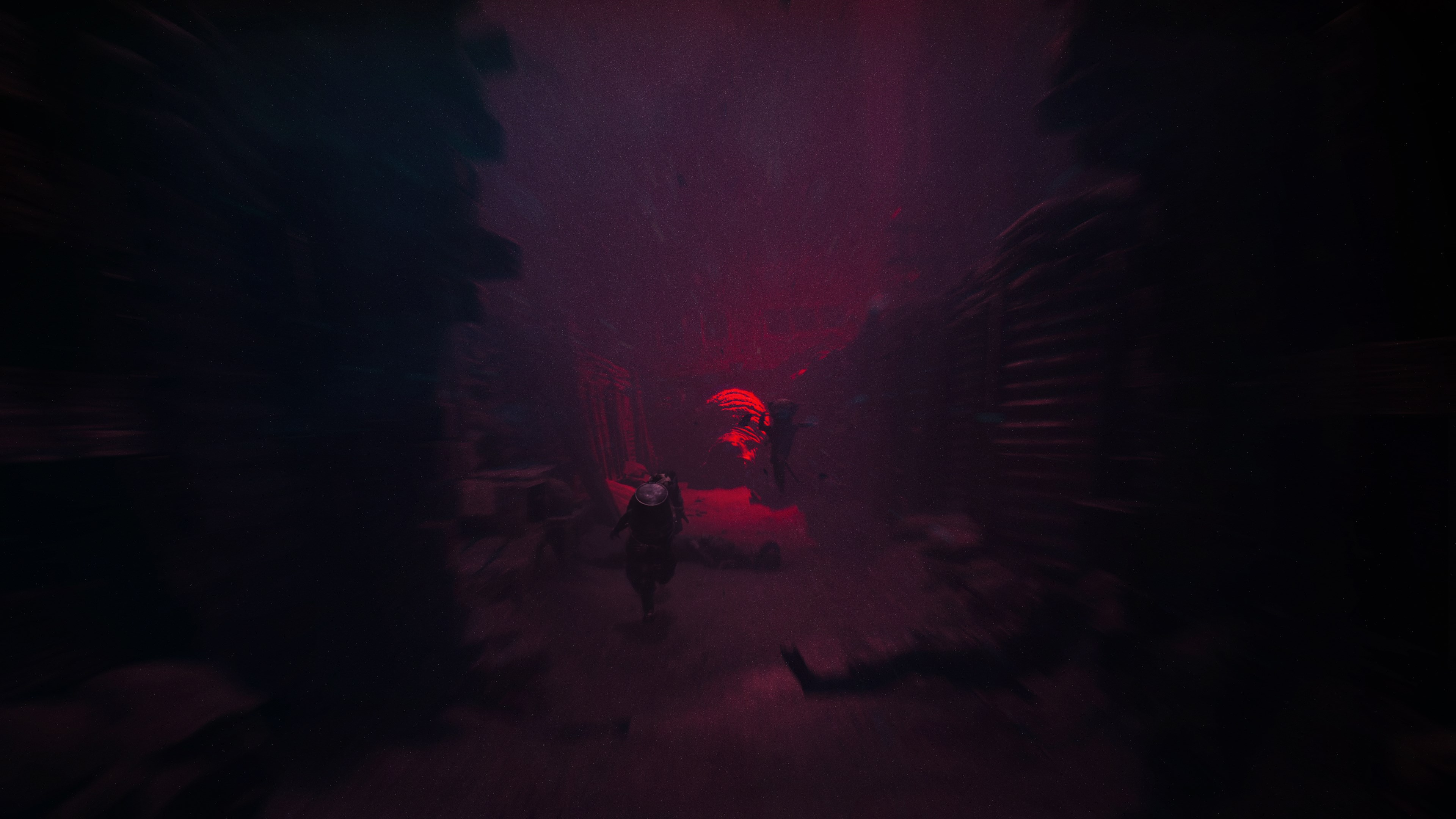 Eine Figur geht durch einen dunklen, rot beleuchteten Tunnel. Die Wände sind rau, ein rotes Leuchten am Ende deutet auf eine Lichtquelle hin.