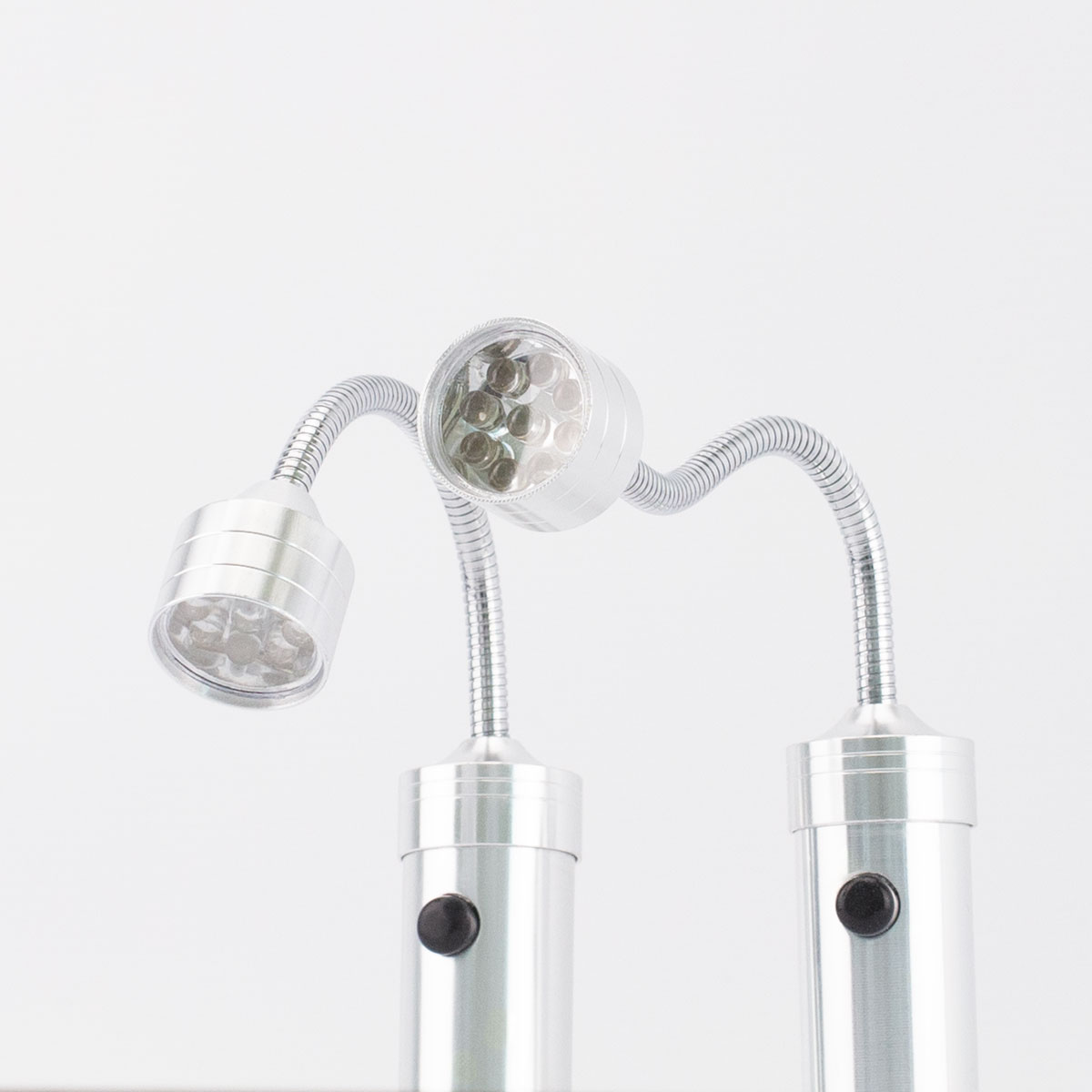Eine silberne LED-Lampe mit drei verstellbaren Köpfen. Jeder Kopf hat mehrere kleine LEDs. Die Lampe steht vor einem weißen Hintergrund.