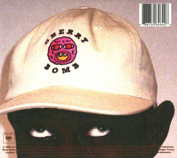 Eine Person mit einer weißen Kappe mit einem rosa und roten Gesichtslogo und dem Wort 'Cherry Bomb'. Die Augen der Person sind sichtbar.