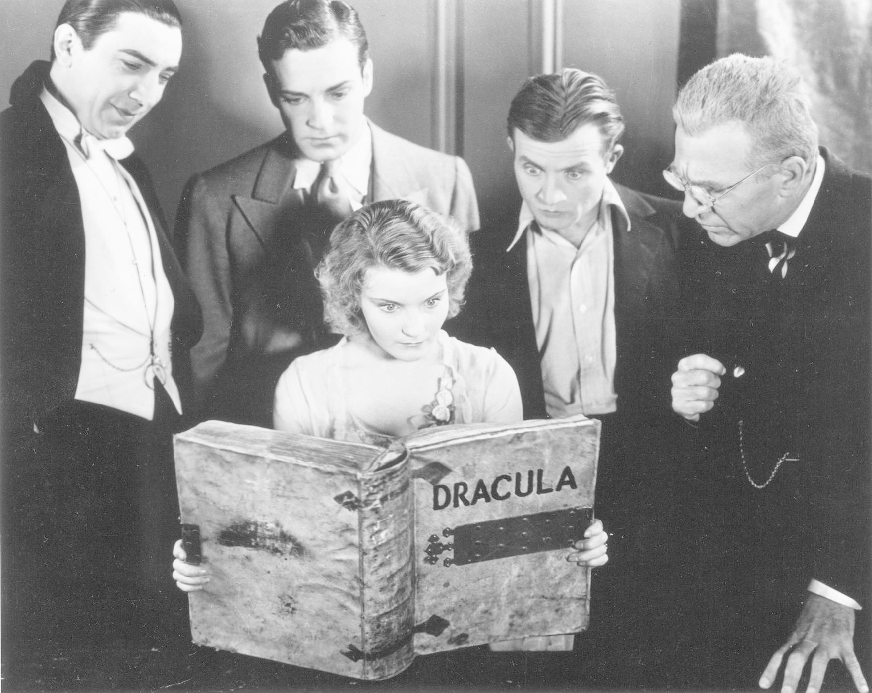 Fünf Personen betrachten ein großes Buch mit dem Titel Dracula. Eine Frau hält das Buch offen, während die anderen mit Neugier blicken.