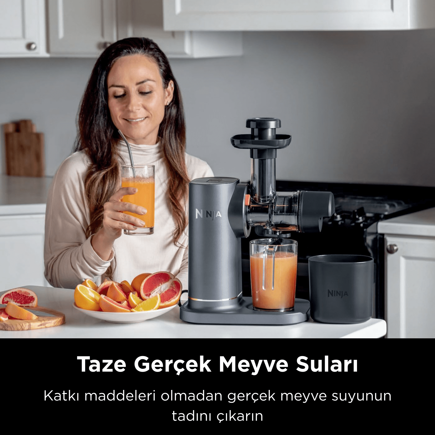 Portakal suyu içen kadın, Ninja sıkacağı, masada meyve dilimleri. Mutfak arka planı, metinde 'Taze Gerçek Meyve Suları' yazıyor.
