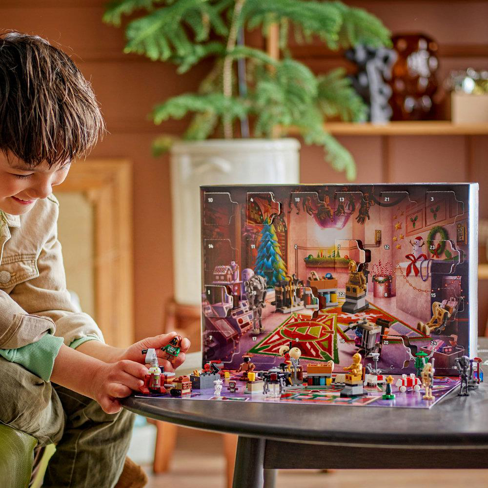 Ein Junge betrachtet einen Lego-Adventskalender. Der Kalender ist geöffnet und zeigt eine Szene mit einem Weihnachtsbaum und Lego-Figuren.