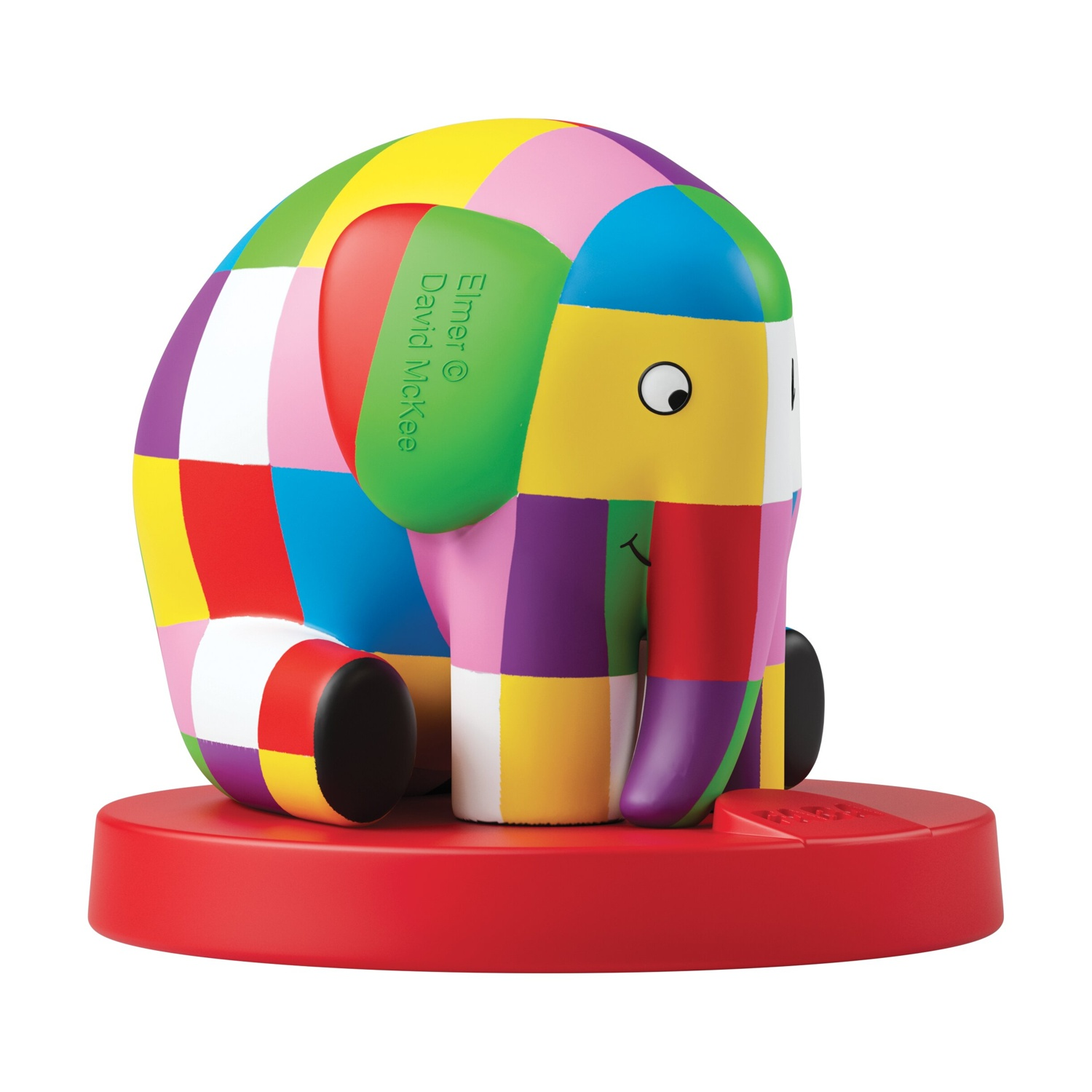 Una colorata statuetta di elefante, design patchwork, seduta su una base rossa. Ha un volto sorridente e sfondo bianco.
