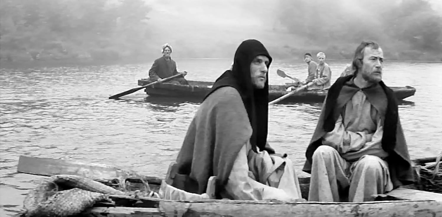Männer in Umhängen rudern in Booten auf dem Wasser. Ein Boot hat drei Männer, ein anderes zwei. Die Szene ist neblig, schwarz-weiß.