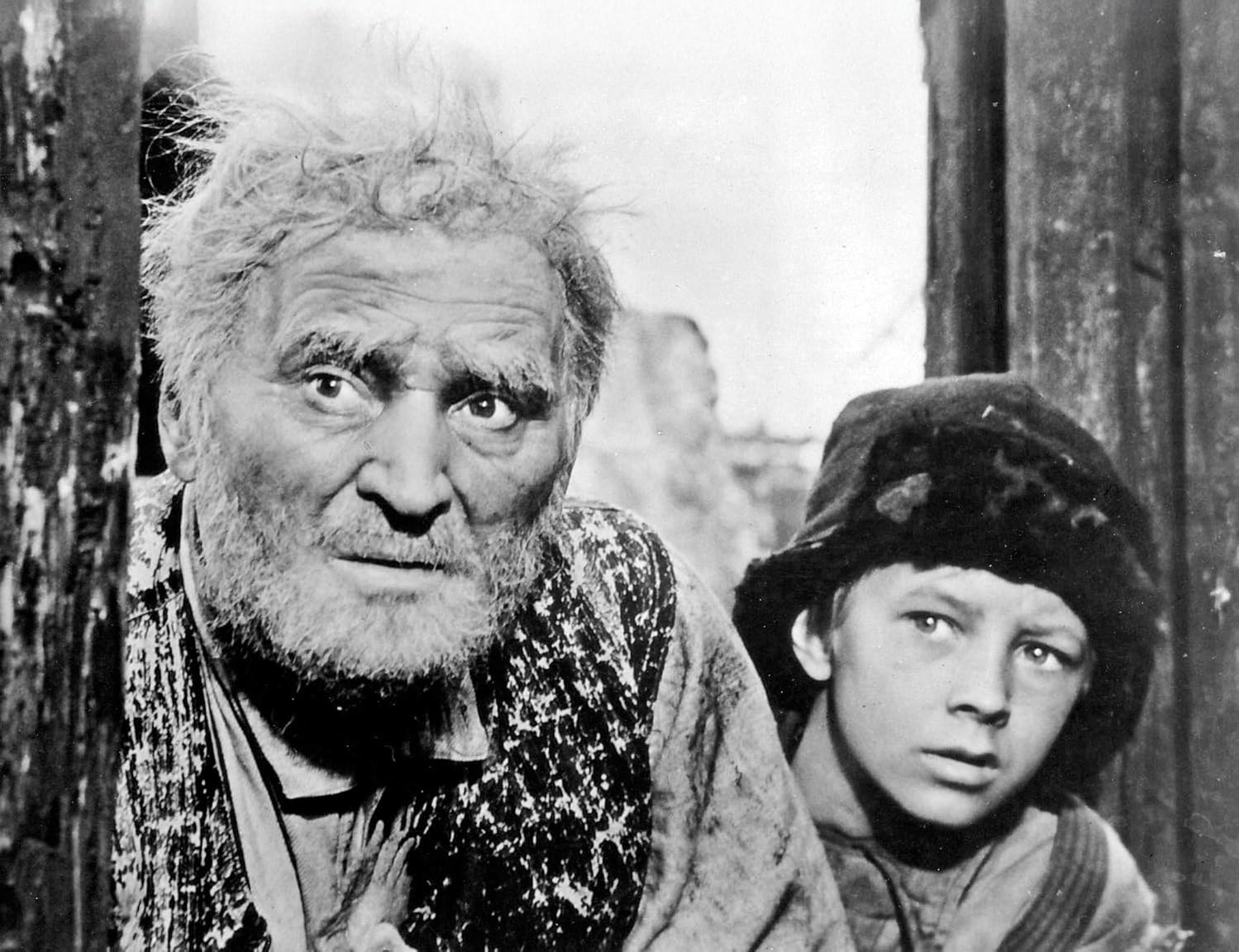 Ein älterer Mann mit Bart und ein junger Junge mit Hut, der den Betrachter ansieht. In Schwarzweiß.