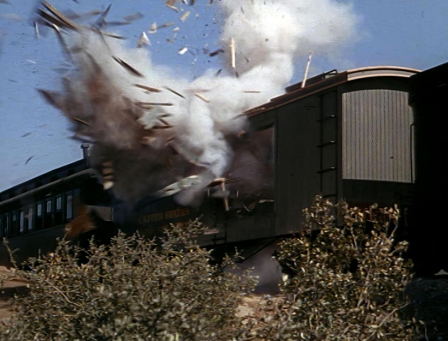 Waggons explodieren mit Rauch und Trümmern vor blauem Himmel. Büsche sind im Vordergrund. Der Zug trägt die Aufschrift "UNITED STATES".