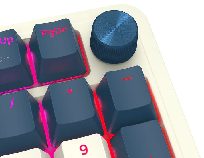 Zbliżenie na klawisze klawiatury. Niebieskie klawisze z białymi literami i różowym podświetleniem. U góry niebieskie pokrętło. Beżowa klawiatura.