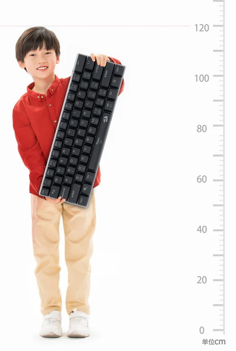 Uśmiechnięte dziecko trzyma czarną klawiaturę. Ma na sobie czerwoną koszulę, beżowe spodnie i białe trampki. Po prawej stronie jest linijka.