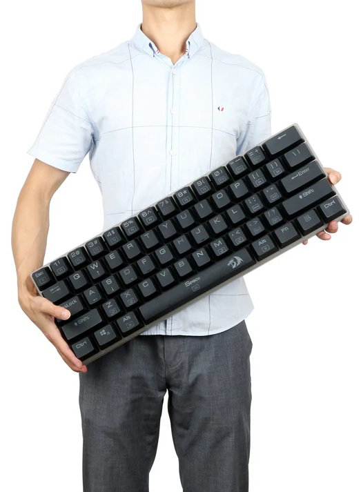 Osoba trzymająca czarną klawiaturę z białymi klawiszami. Osoba ma na sobie jasnoniebieską koszulę i szare spodnie. Białe tło.