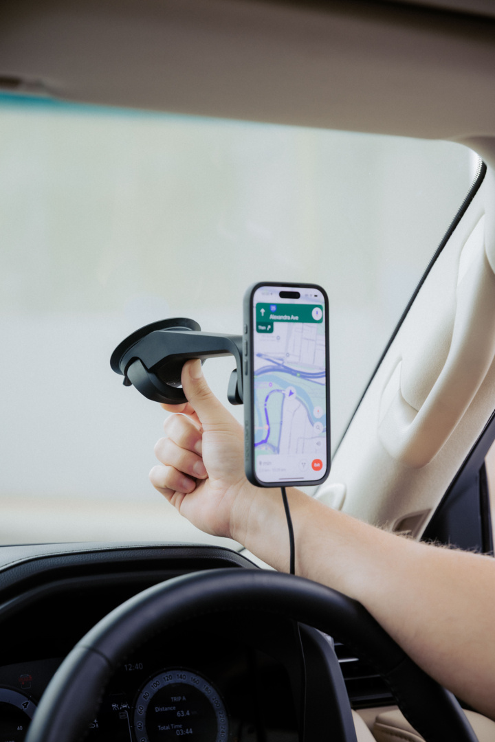 Mano che tiene un telefono con mappa, montato sul parabrezza di un'auto. Interni dell'auto visibili.
