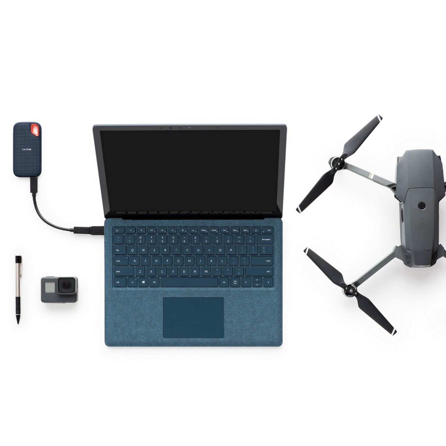 Una laptop, un dron, una cámara, un bolígrafo y un disco duro externo están sobre una superficie blanca.