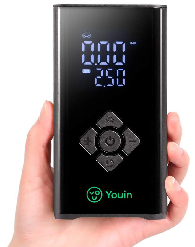 Una mano sostiene un compresor de aire Youin negro. La pantalla muestra 0.00 y 2.50. Botones: más, menos, encendido/apagado y ajustes.