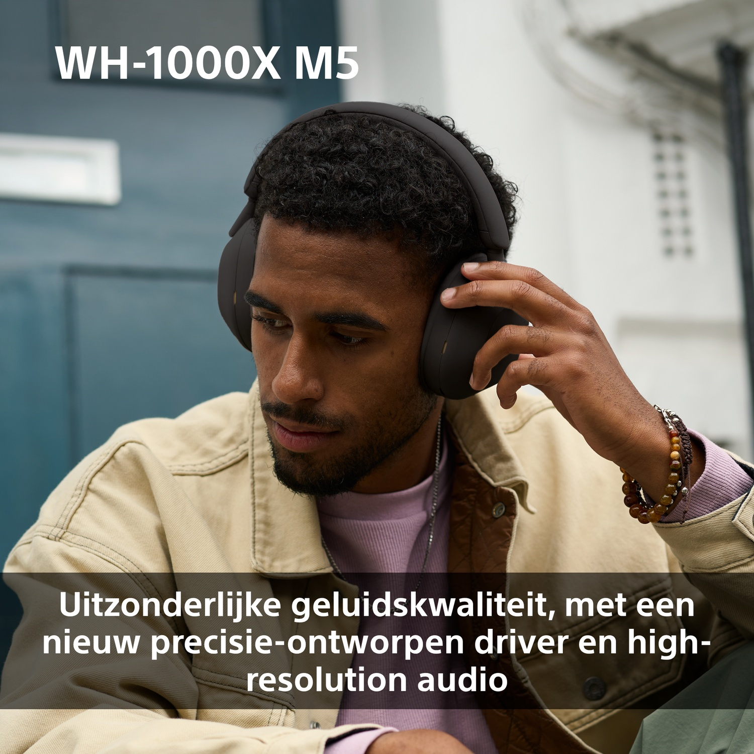 Un homme portant un casque noir. Il porte une veste beige et une chemise rose. Le texte dit 'WH-1000X M5'.
