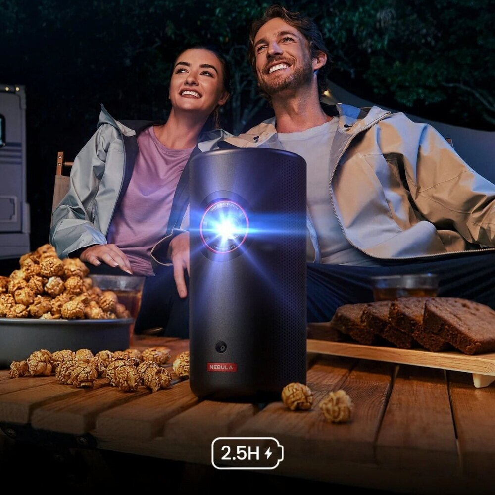 Para ogląda projektor z popcornem i chlebem na stole. Czarny projektor jest pośrodku z jasnym światłem.